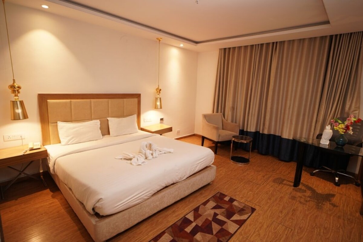 A hotel room with a large bed, bedside tables, a desk, a chair, and a curtain.