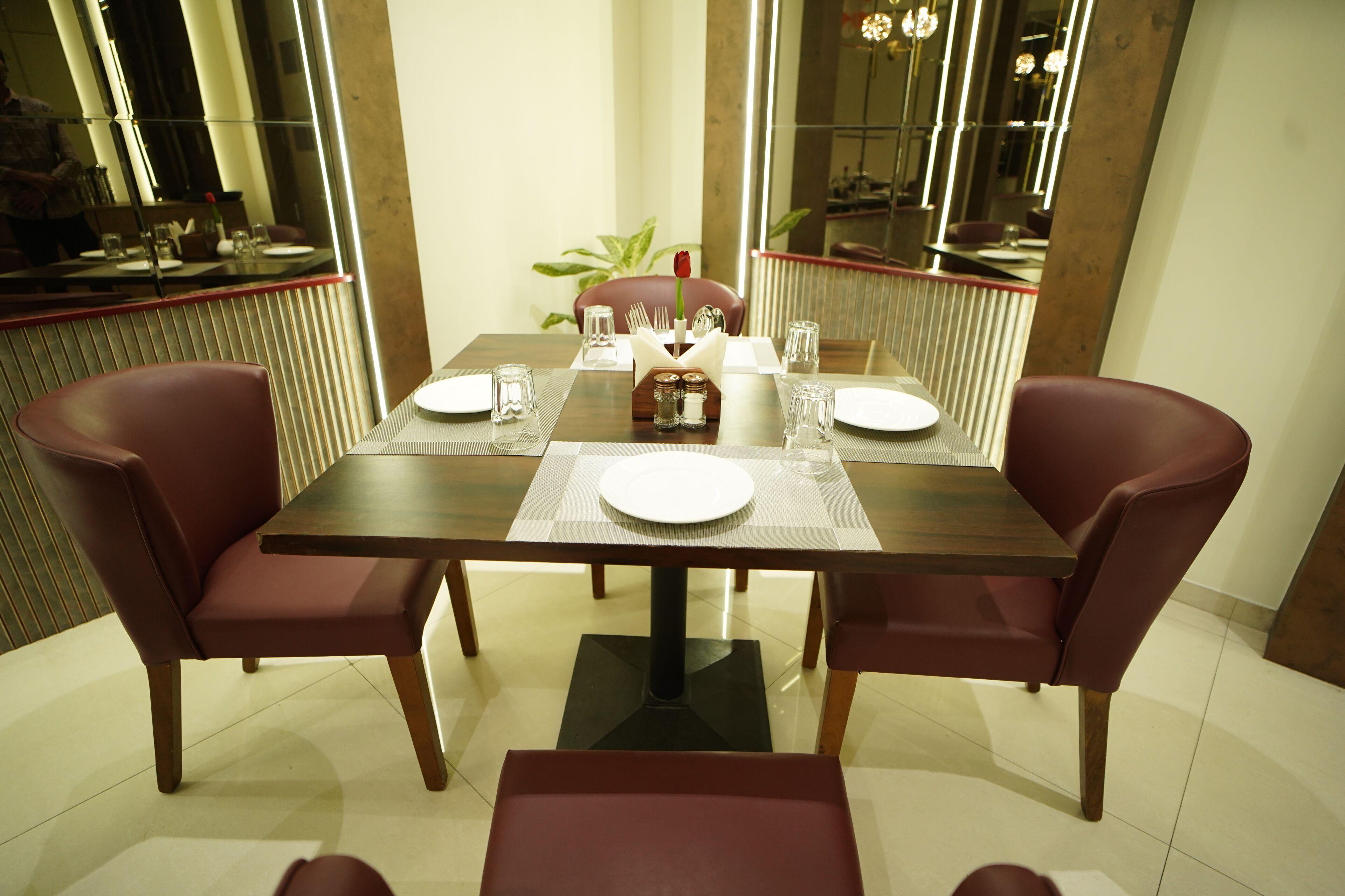 A dining table set for four with a central vase, surrounded by red upholstered chairs.