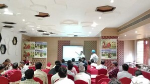 A conference room with a presentation screen, red chairs, and a speaker at the front. - Hotel Amora (Rajnandgaon)