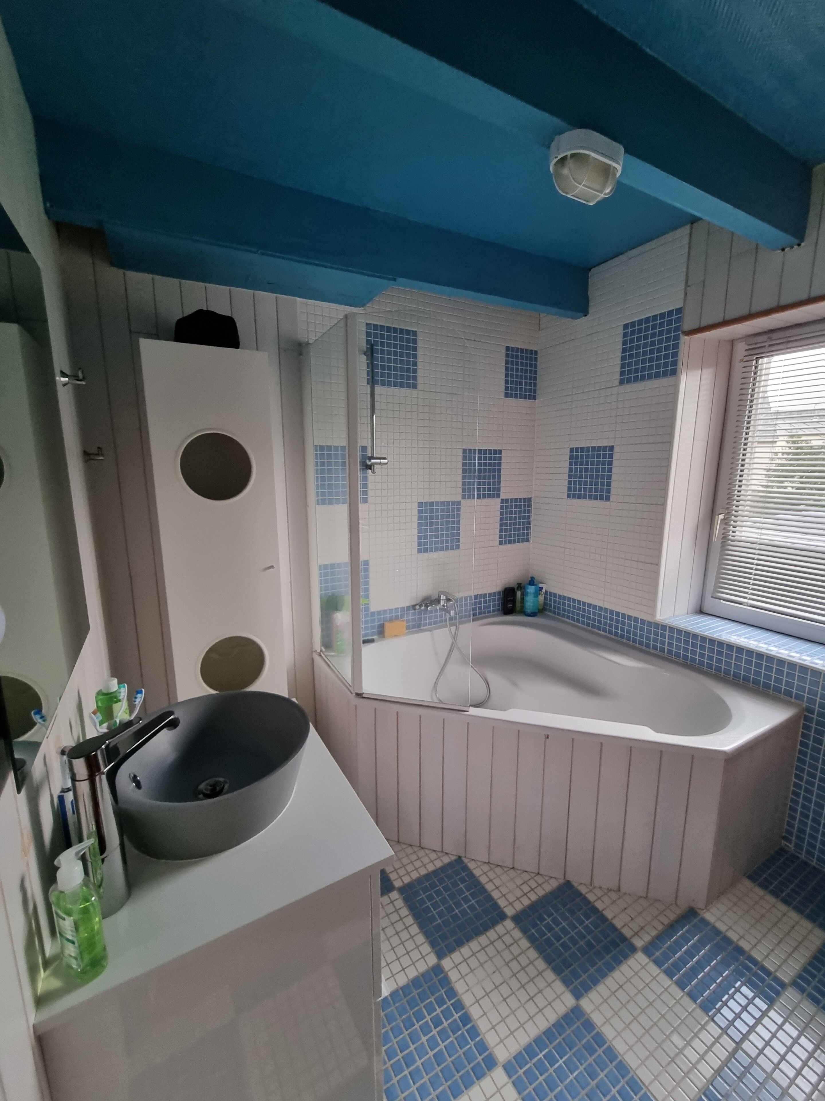 A bathroom with a white sink, a bathtub, and a window with blinds.