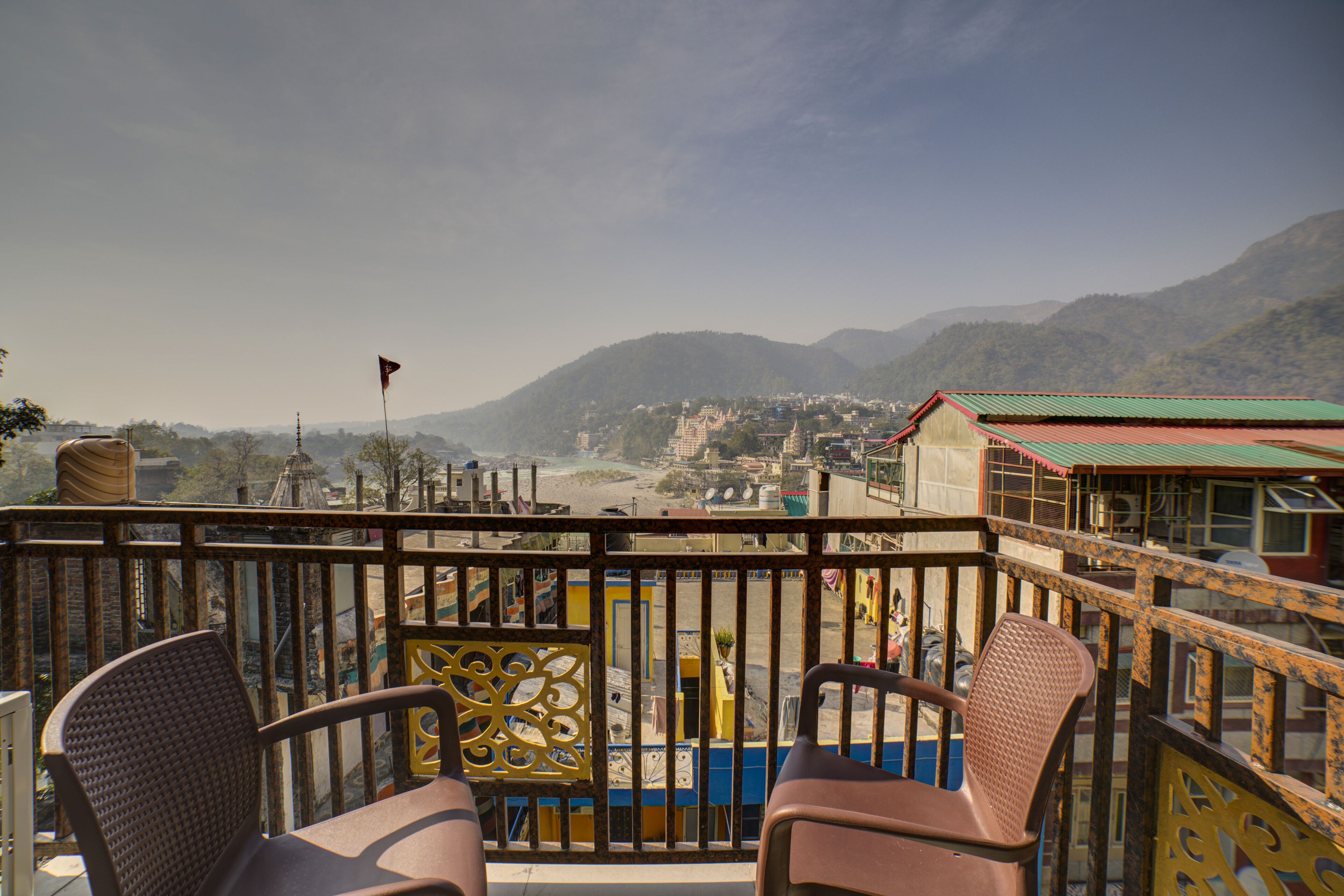 A balcony with two chairs, a view of a town and mountains in the background.