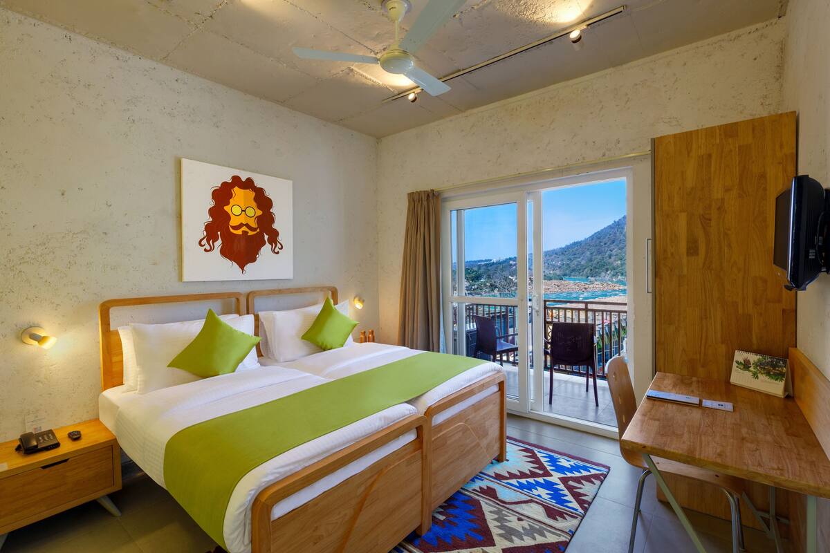 A hotel room with a bed, a desk, a chair, a balcony with a view, and a ceiling fan.