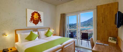A hotel room with a bed, a desk, a chair, a balcony with a view, and a ceiling fan.