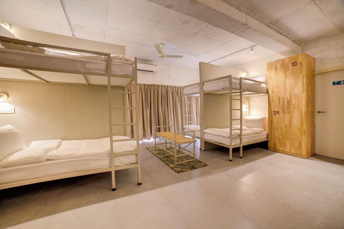 A dormitory room with bunk beds, a wooden wardrobe, and a ceiling fan.