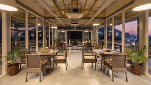 Un espace extérieur abrité, aménagé pour les repas, avec des meubles en osier et de grandes fenêtres offrant une vue sur la ville.