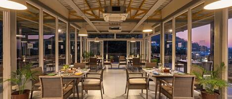 A covered outdoor dining area with wicker furniture and large windows offering city views.