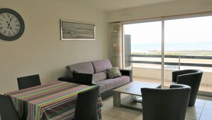 A living room with a sofa, a coffee table, and a dining table with chairs. There is a large window with a view of the sea. - Apartment with terrace, WIFI and parking in Perros-Guirec (Perros-Guirec)