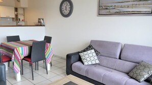 A modern living room with a sofa, a coffee table, and a dining area with chairs and a striped tablecloth. - Apartment with terrace, WIFI and parking in Perros-Guirec (Perros-Guirec)