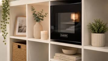 Uma sala de estar moderna com uma TV de tela plana em uma prateleira branca, adornada com objetos decorativos como um vaso, uma vela e livros.