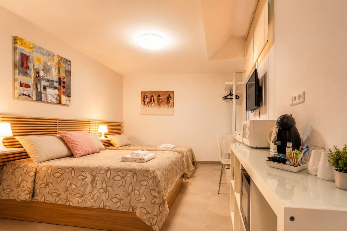 Een hotelkamer met een bed, nachtkastje, lamp, kunstwerk en een kitchenette.