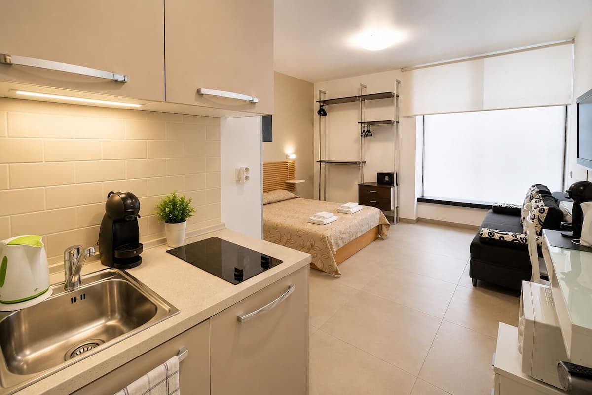 Een moderne hotelkamer met kitchenette, een bed met beigekleurige sprei, een nachtkastje, een televisie en een sofa.