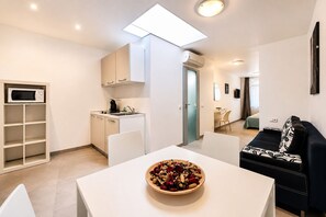 Un apartamento moderno con kitchenette, un comedor con un tazón de fruta, un sofá blanco y negro estampado, y vista al salón.