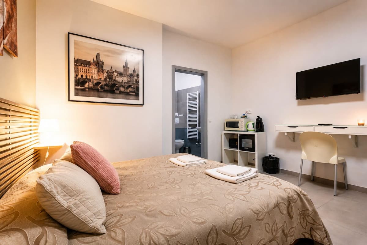 Quarto de hotel com uma cama, uma escrivaninha, uma televisão e uma fotografia da paisagem urbana.