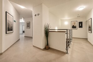 Un couloir d’hôtel orné d’œuvres d’art encadrées, un comptoir de réception et des panneaux indicateurs.