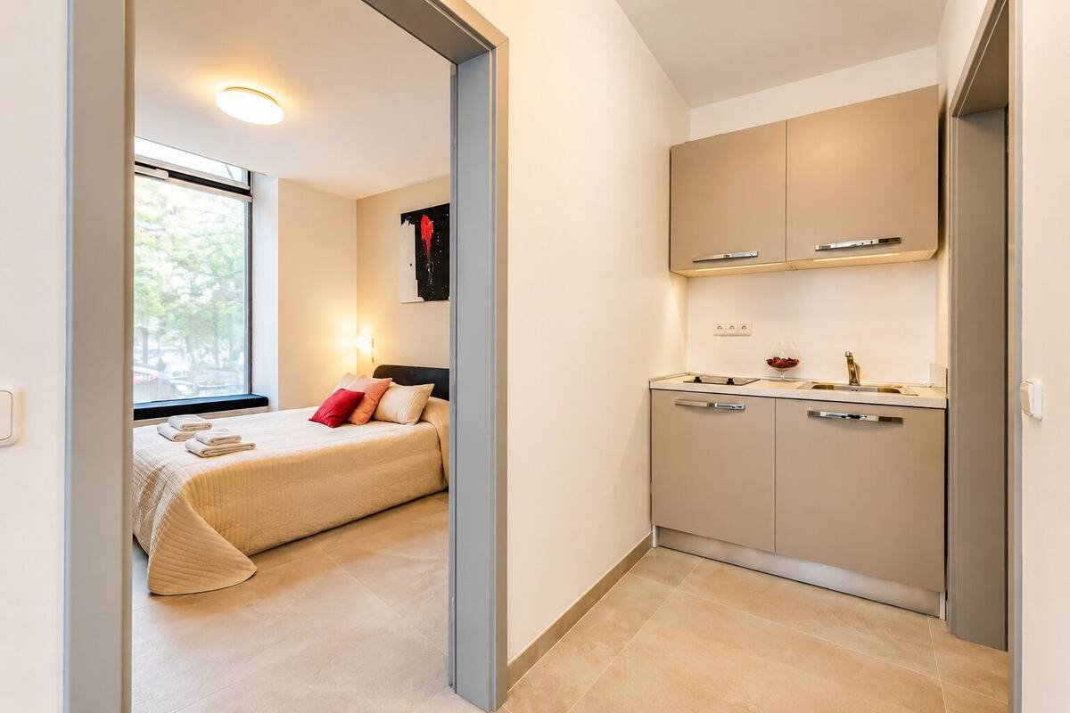 Een slaapkamer met een bed, kussens, een raam en een nachtkastje.