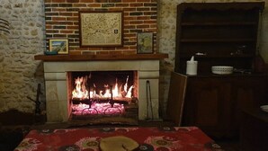 A fireplace with a burning fire, a framed map on the mantel, and a table with a red tablecloth. - A dream holiday in the heart of nature in a historic setting (Beaumont-Louestault)