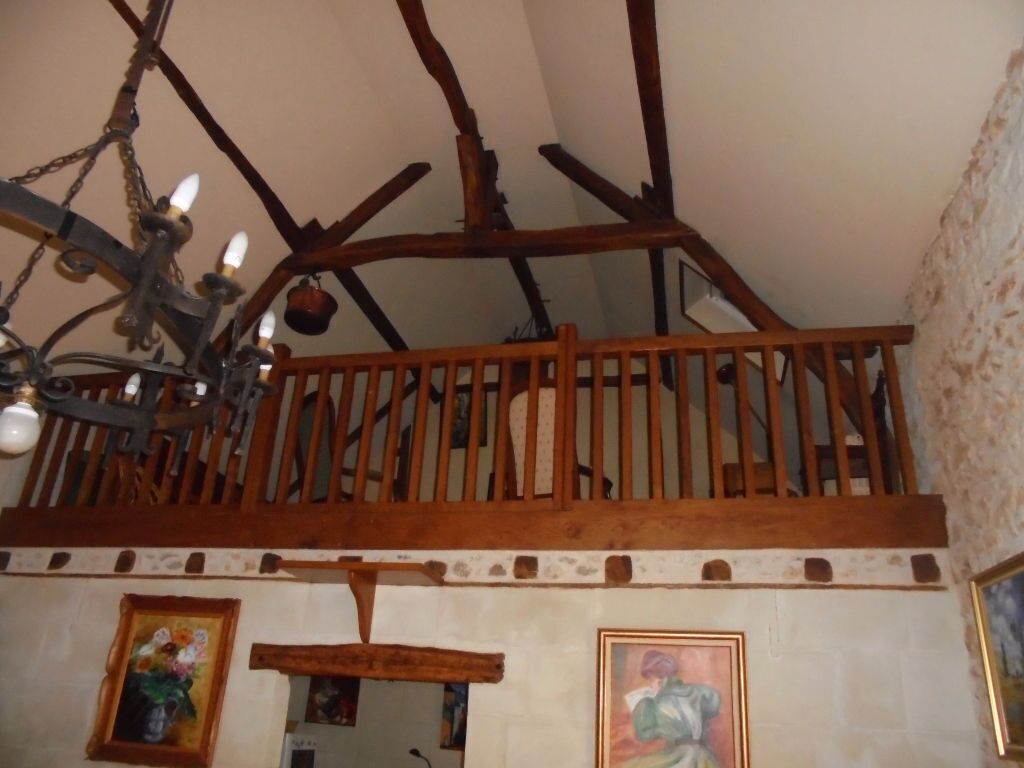 Un interior rústico con vigas de madera a la vista, un balcón de madera y una araña.