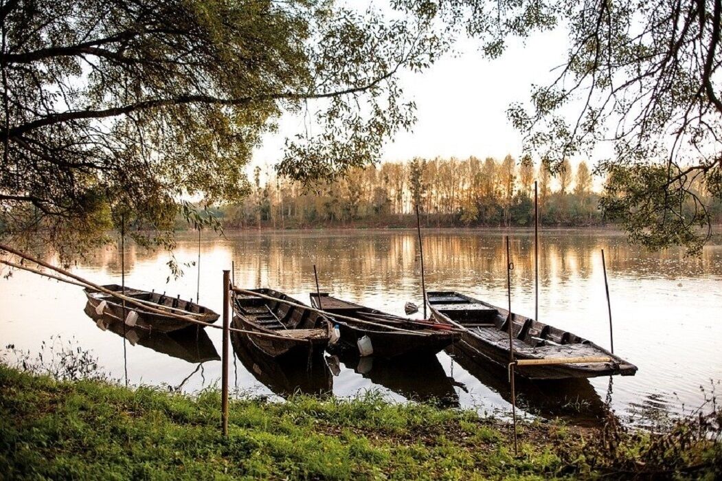 Un lago tranquillo con tre barche di legno ormeggiate a un molo.