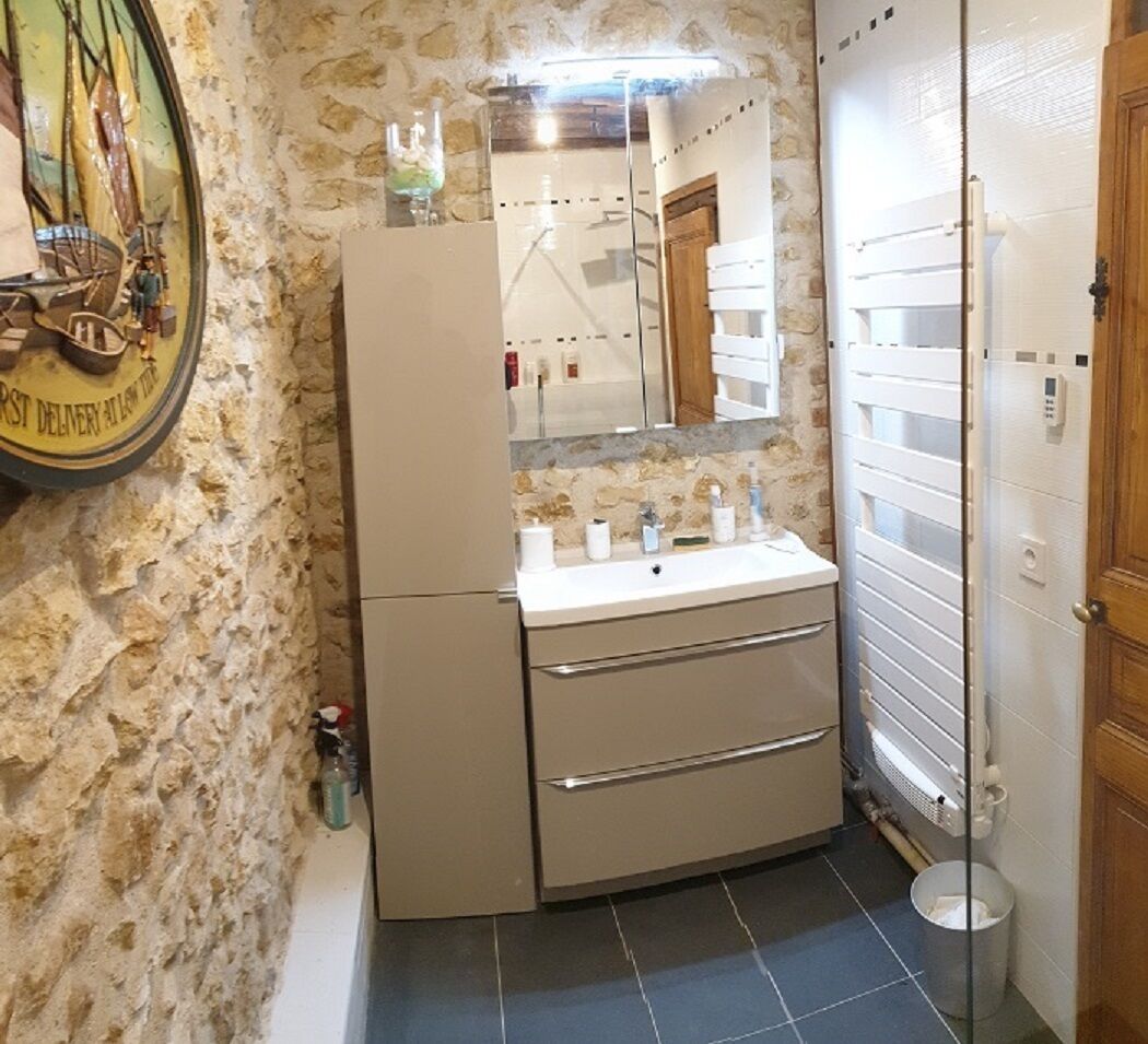 A bathroom with a stone wall, a sink with a mirror, a wooden door, and a small shelf with toiletries.