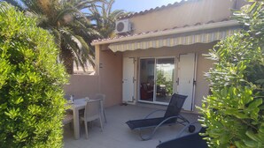 Un patio con una mesa y sillas, una silla azul y una puerta corrediza de vidrio que da a un área cubierta.