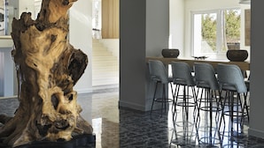Un interior moderno con una gran escultura de madera, una zona de bar con taburetes y vistas a través de un amplio ventanal.