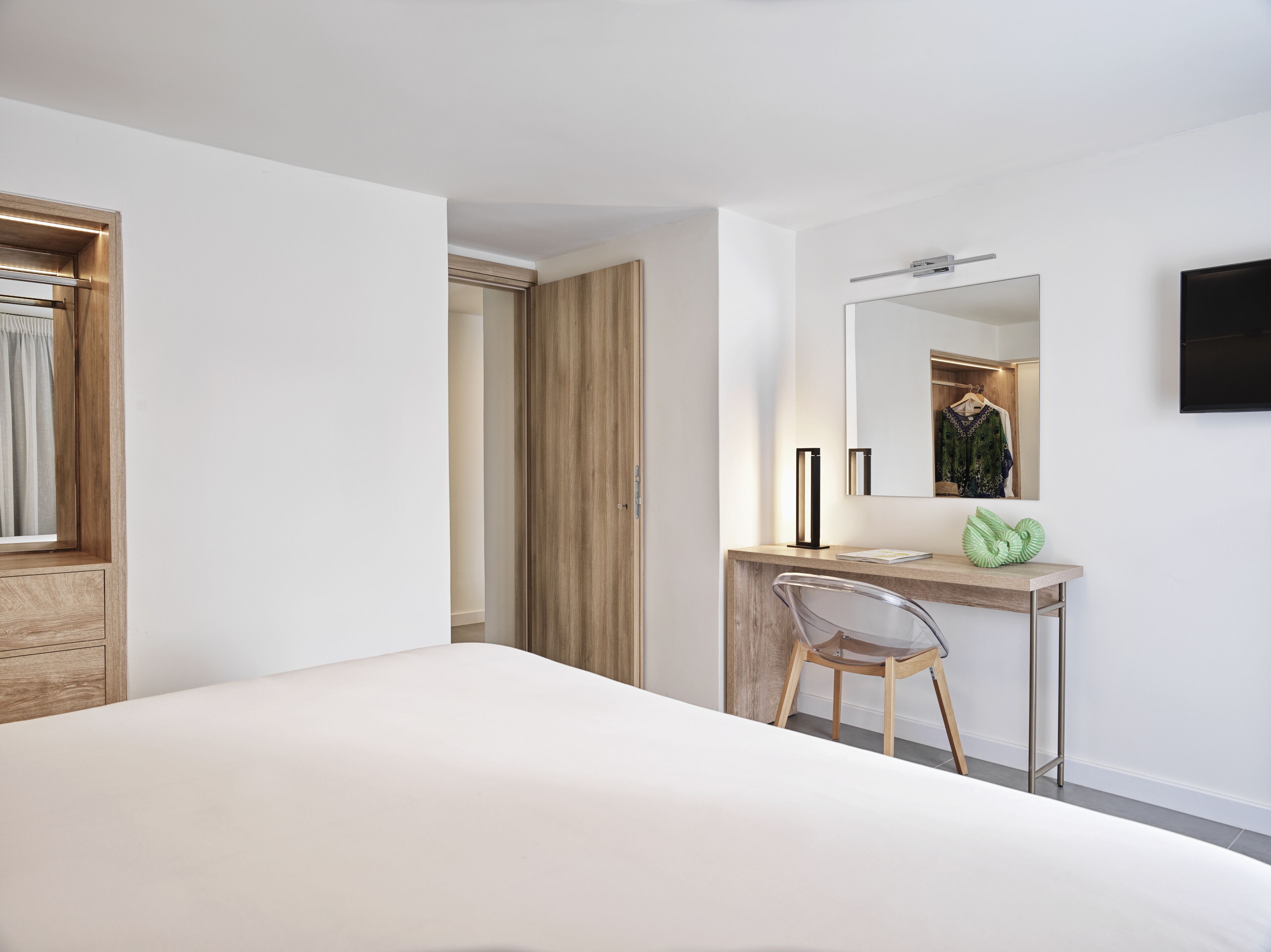 A modern hotel room with a large bed, a wooden desk, a chair, a mirror, and a TV mounted on the wall.