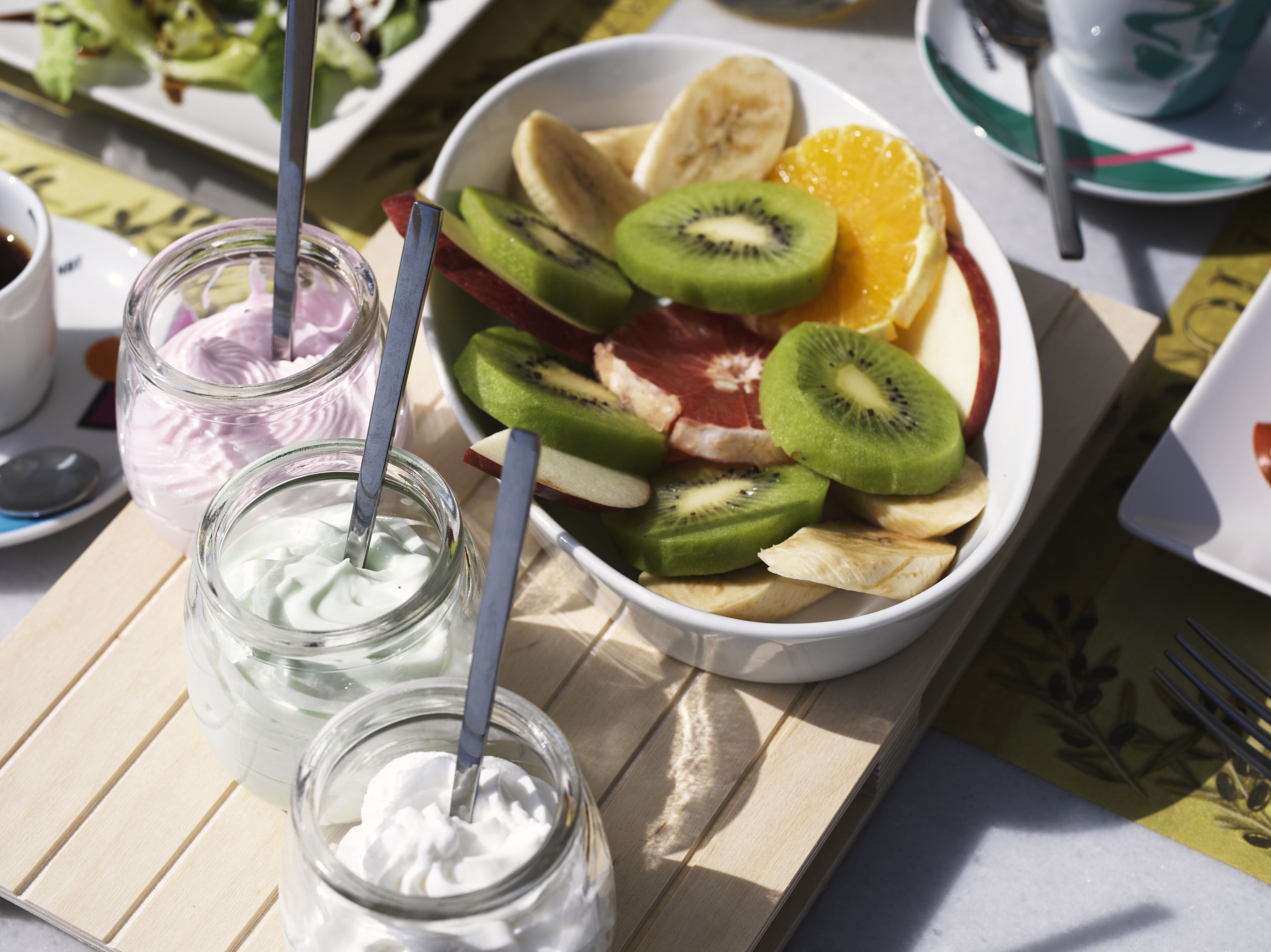 A table with a bowl of fruit, two jars of whipped cream, and a cup of coffee.