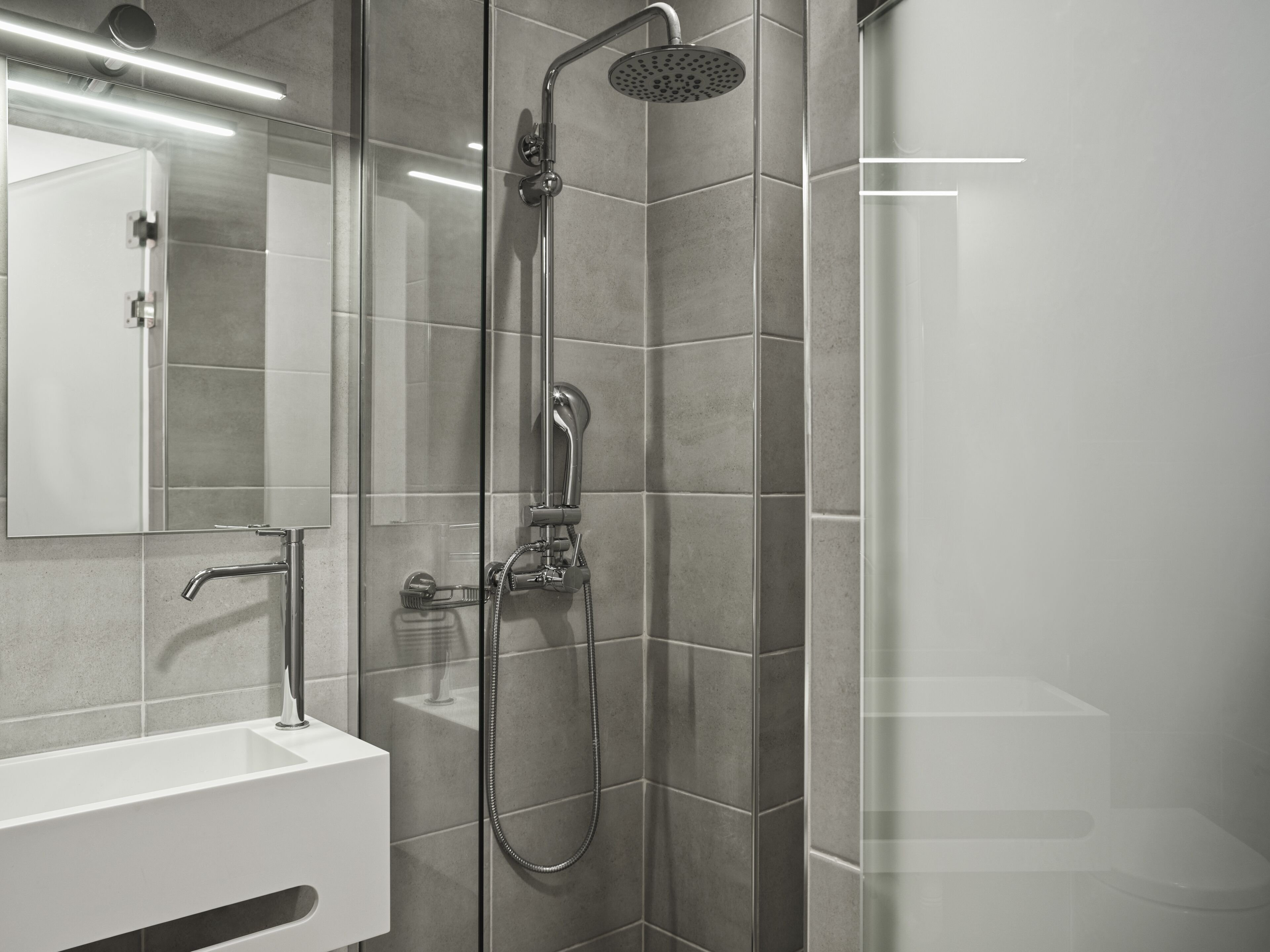 Un baño moderno con cabina de ducha de vidrio, un lavabo blanco y un espejo.