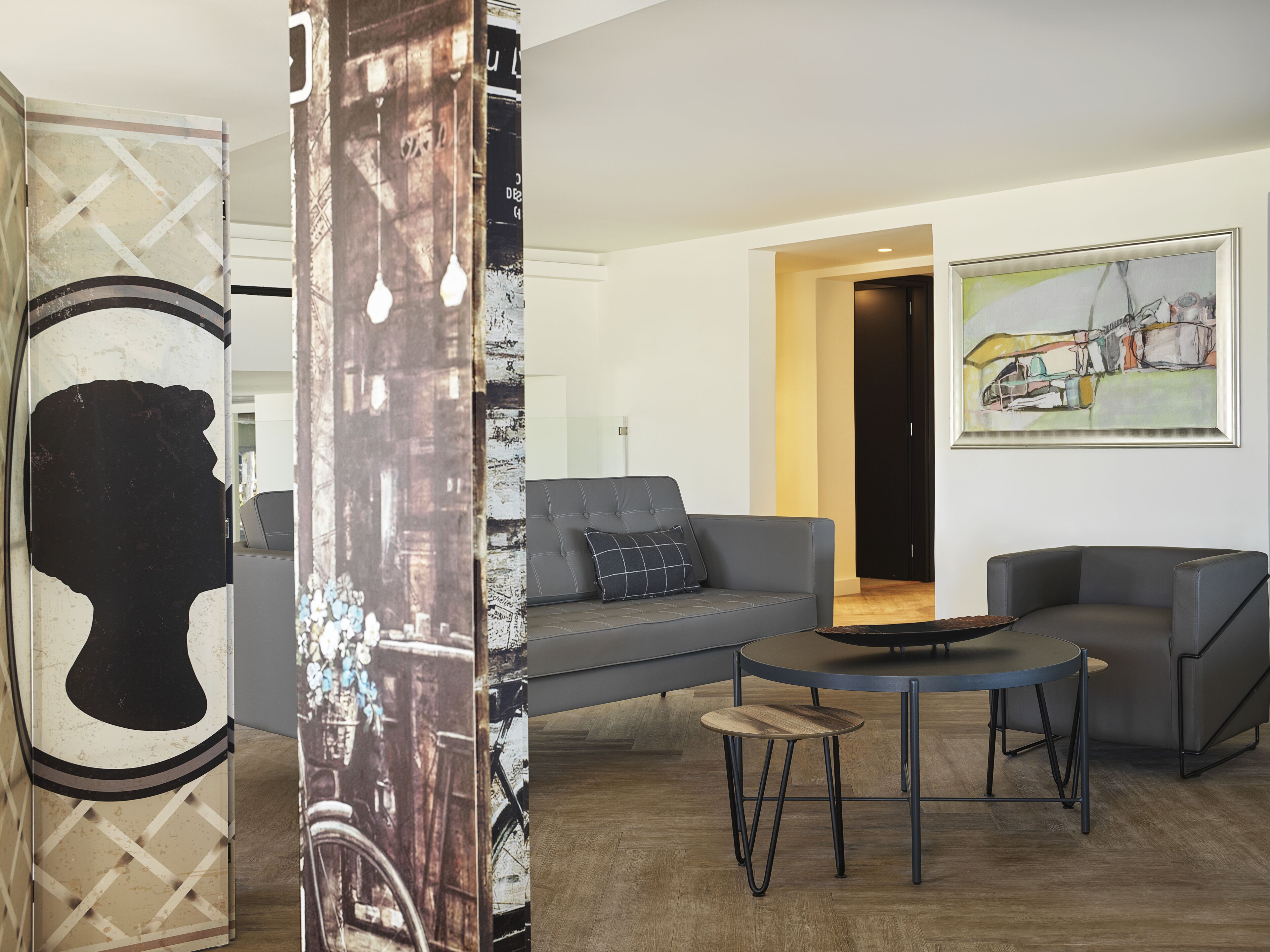 Een moderne woonkamer met een grijze bank, een ronde salontafel en een schilderij aan de muur.