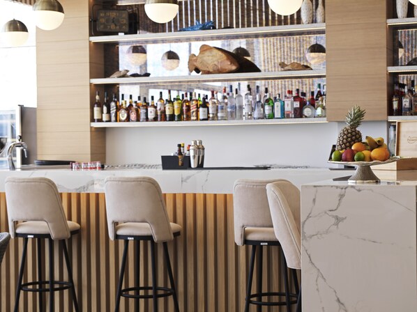 A bar area with three bar stools, a marble countertop, and shelves stocked with various bottles.