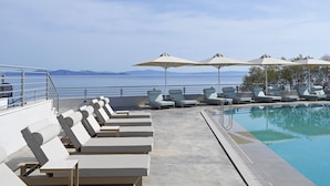 Zona junto a la piscina con sillones de descanso y sombrillas, con vista a un cuerpo de agua y tierra distante.