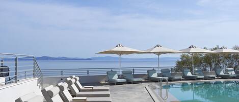 Un espace aménagé au bord de la piscine, avec des chaises longues et des parasols, offrant une vue sur une étendue d’eau et sur la terre ferme au loin.
