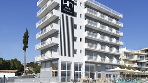 A modern hotel with a rooftop pool, multiple balconies, and a clear blue sky.