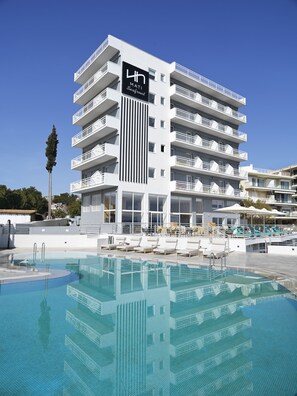A modern hotel with a rooftop pool, multiple balconies, and a clear blue sky.