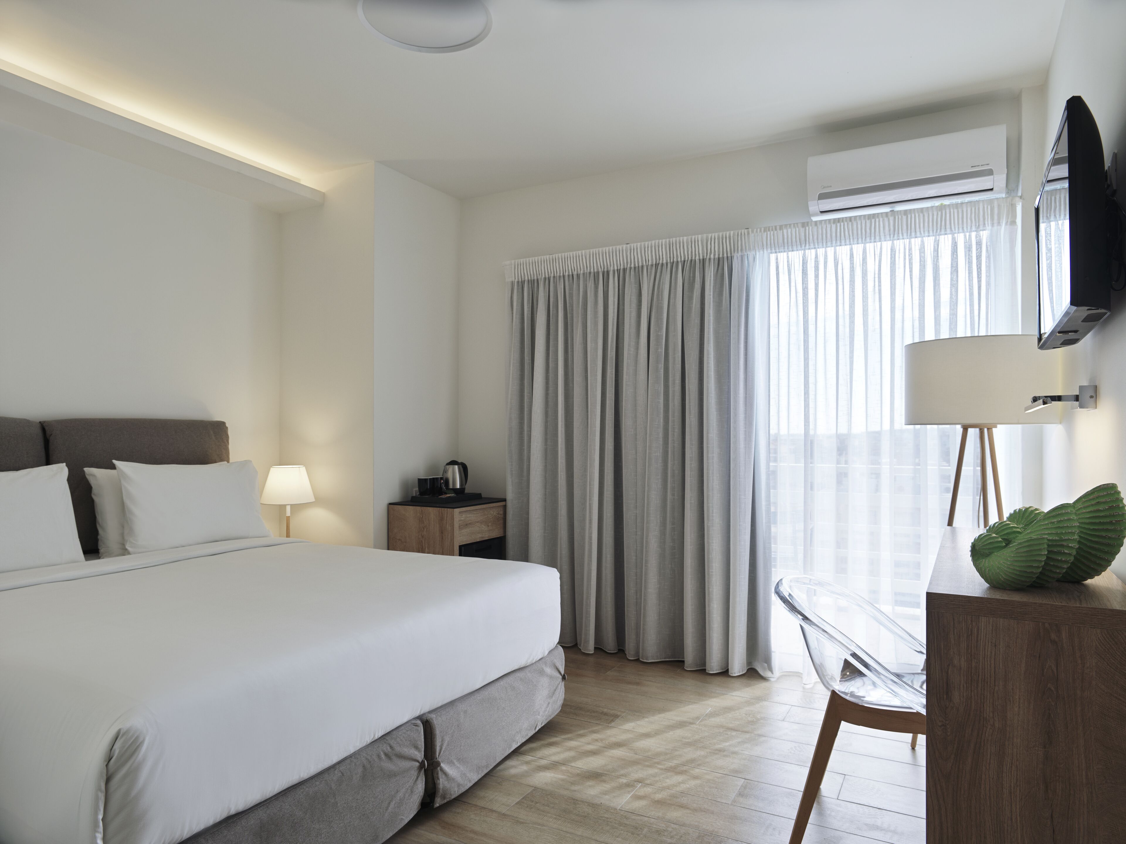 A modern hotel room with a large bed, a desk, a lamp, and an air conditioning unit.