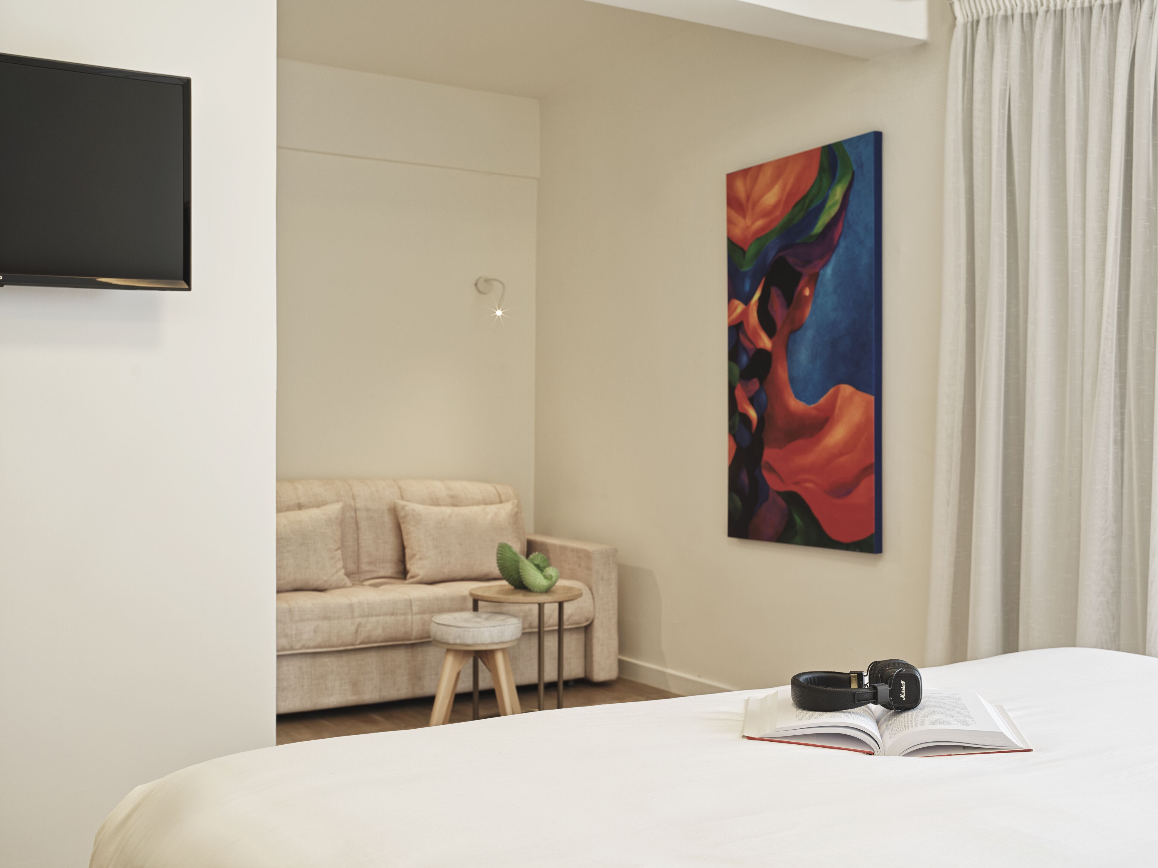 Une chambre d’hôtel moderne, équipée d’un lit, d’une petite table ronde, d’un canapé et d’un tableau abstrait aux couleurs vives accroché au mur.