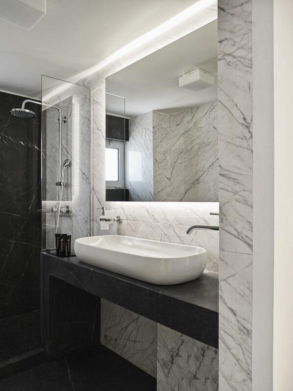 Un baño moderno con un espejo grande, un lavamanos blanco y una zona de ducha.