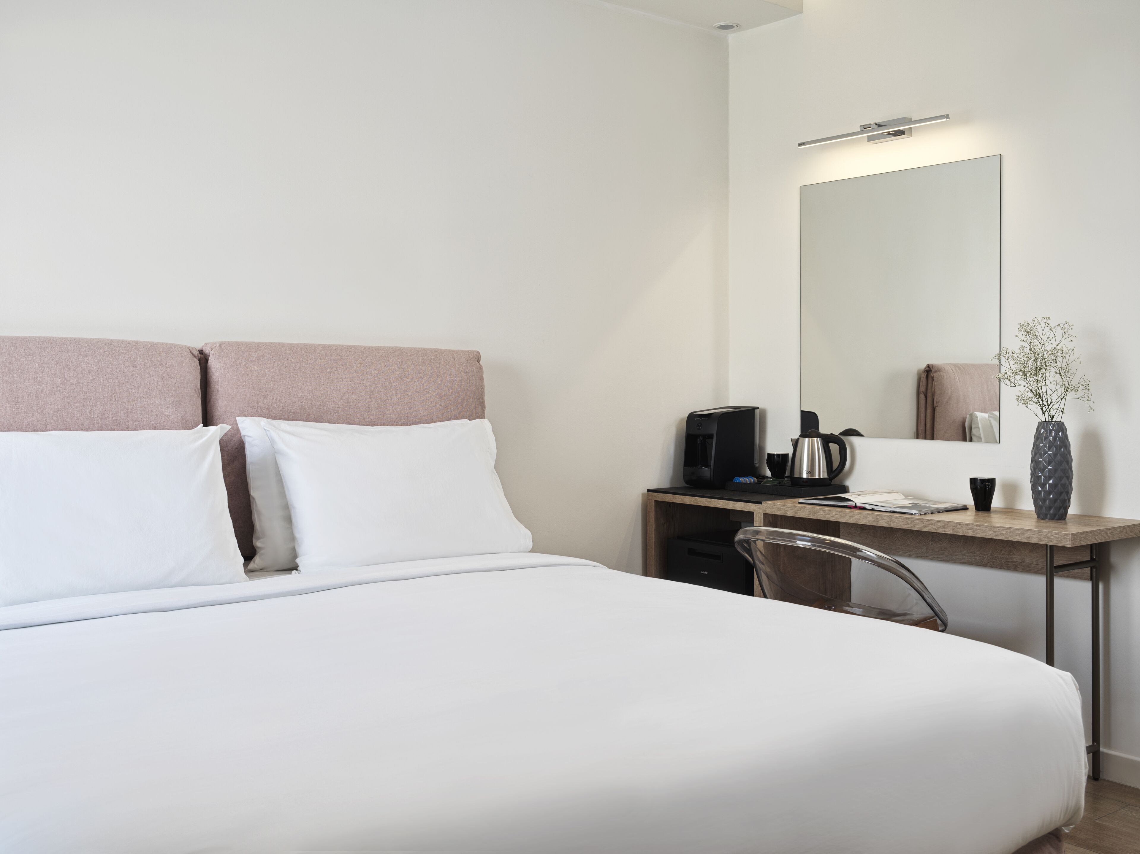 Een hotelkamer met een bed, een bureau met koffiezetapparaat, een spiegel en een vaas met bloemen.