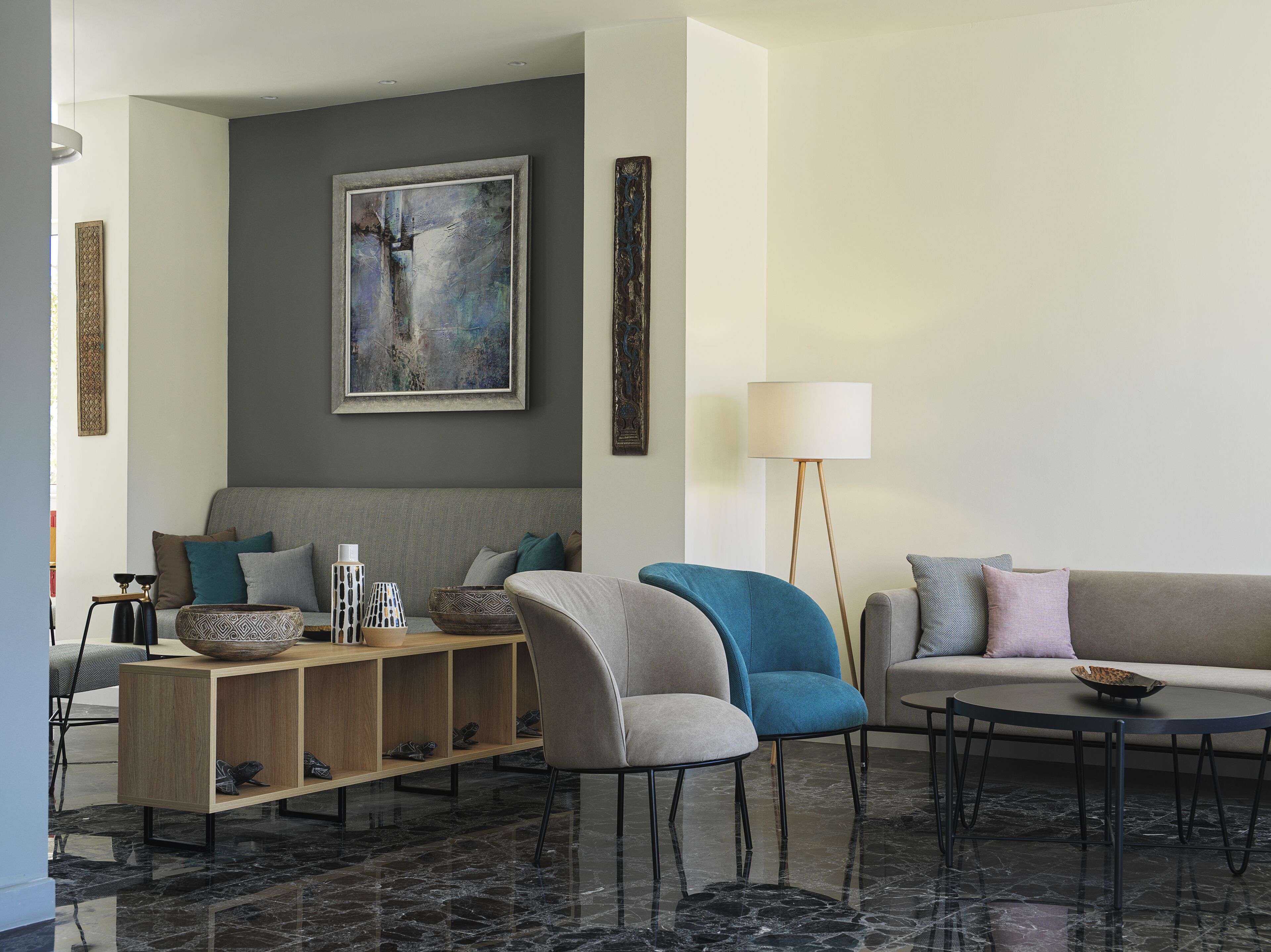 Un salon moderne avec un canapé gris, un fauteuil bleu, une console en bois et un lampadaire.