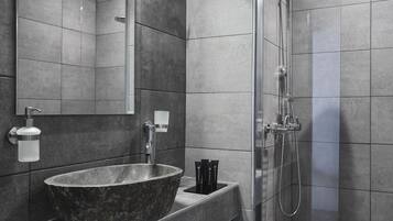 Un baño moderno con un lavabo grande de piedra oscura, un cabezal de ducha de mano y un espejo sobre el lavabo.