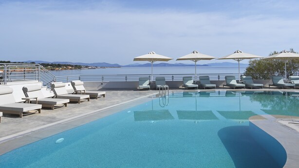 A pool area with lounge chairs and umbrellas, a clear sky, and a view of the water.