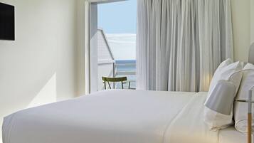 A bedroom with a large bed, a view of the sea through a window, and a chair by the window.