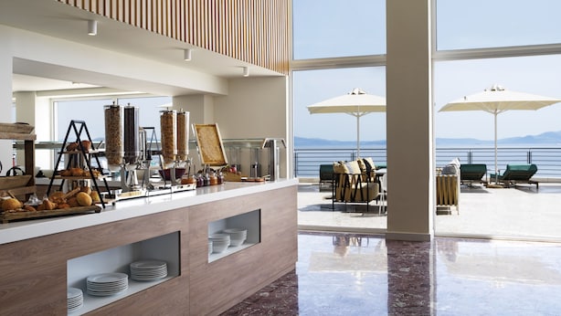 Una barra de desayuno moderna con vista al mar, asientos al aire libre con sombrillas y techo de madera.