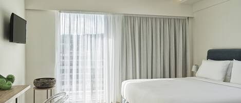 A modern hotel room with a large bed, a desk with a chair, and a television on the wall.