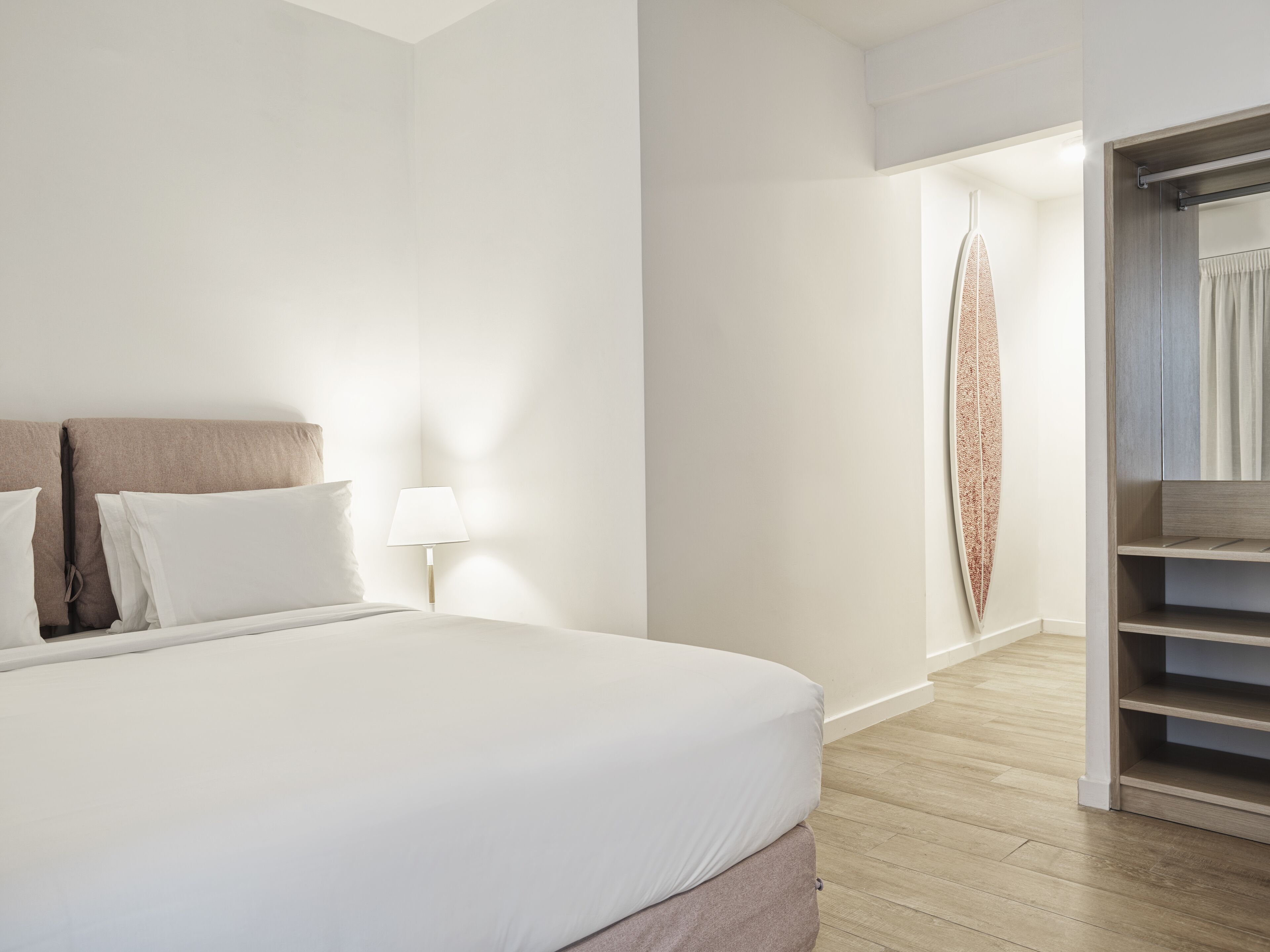 Et moderne hotelværelse med en stor seng, en senelampe og trægulv.