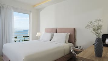 Une chambre d’hôtel avec un grand lit, une table de chevet, une lampe, un vase de fleurs et une vue sur la mer par la fenêtre.
