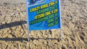 Schild am Strand mit Preisen für Wassersportaktivitäten.