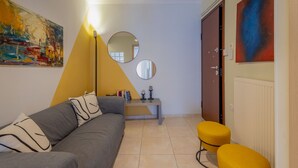 Un salon moderne avec un canapé gris, un mur d’accent jaune, un miroir rond et une porte donnant sur une autre pièce.