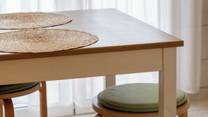 Une table en bois, agrémentée de sets de table tressés et de tabourets rembourrés de couleur verte.