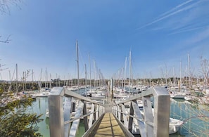 Ein Yachthafen mit zahlreichen vertäuten Booten, einer Fußgängerbrücke und wolkenlosem Himmel.